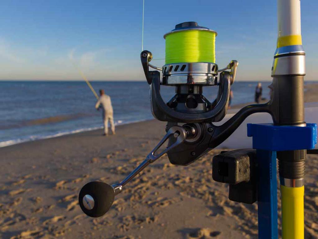 A close-up of a surf fishing rod, with a surf fisherman in the background