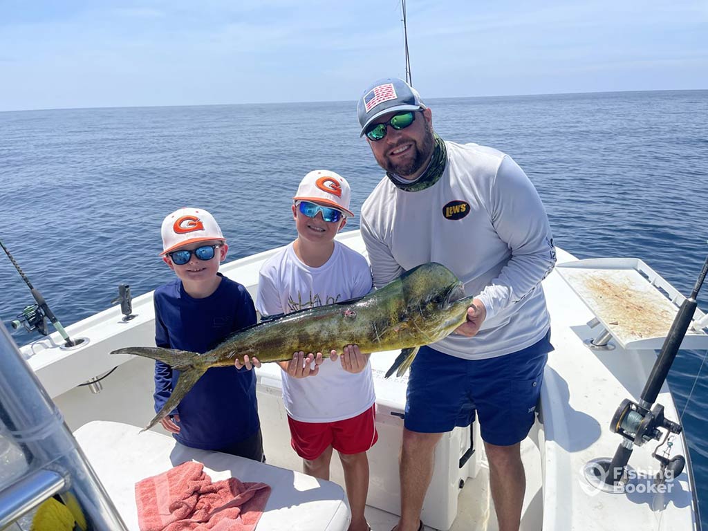 A man and two boys standing on the bow of a fishing charter out of Panama City, holding a Mahi Mahi between them