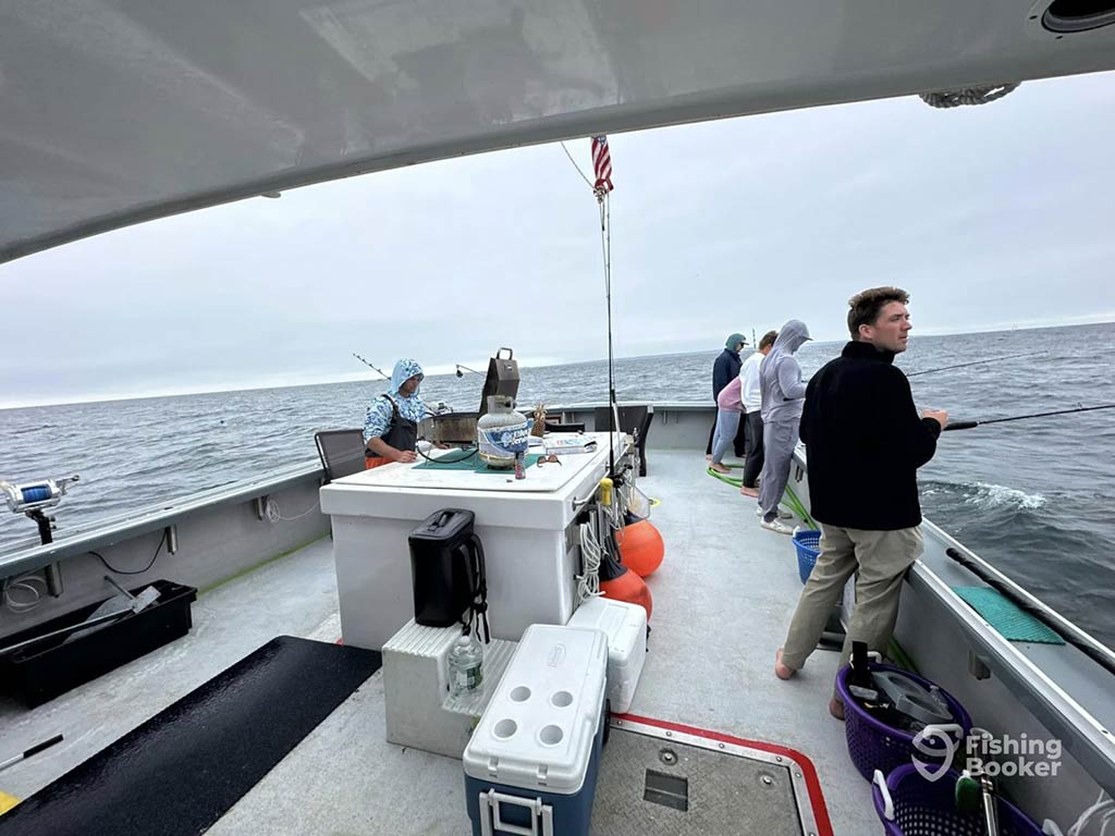 A view of the deck of a fishing boat in Maine on a cloudy day with a number of anglers practicing bottom fishing