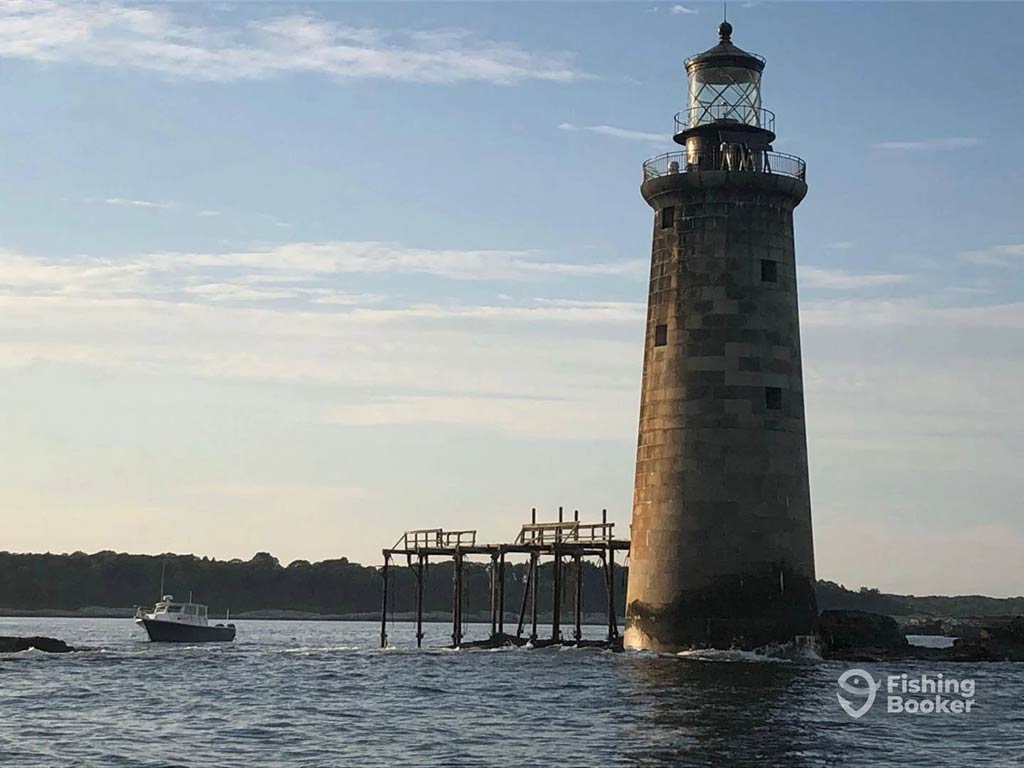 A view across the water from a boat towards a lighthouse seemingly in the middle of the water in Maine on a clear day